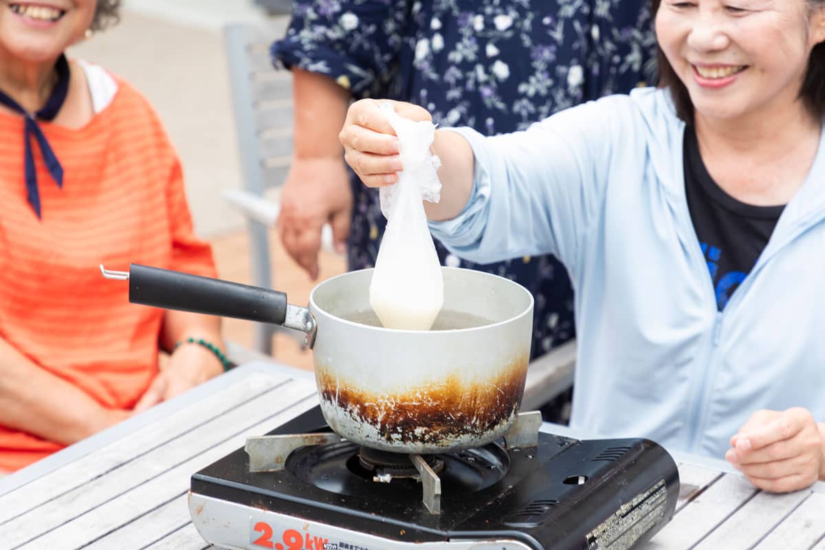 耐熱ポリ袋に米と水をいれたものを、ガスコンロにセットされた鍋で湯煎して炊飯している。