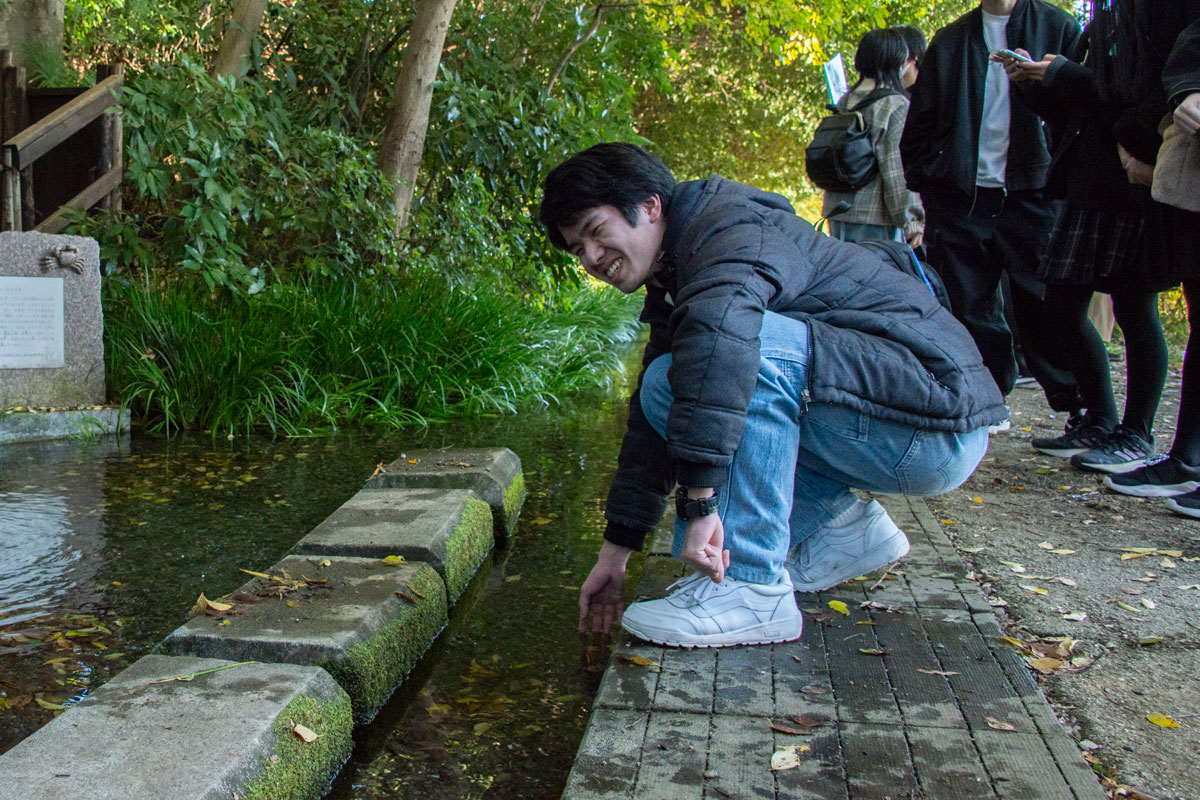 ママ下湧水の湧き水にそっと片手を差し入れ、水の温度を確かめている男性。水面に湧水の波紋が見える。