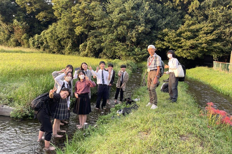 田んぼ脇の水路に足をひたしながら、高校生たちが思い思いのポーズをして写っているスナップ写真。